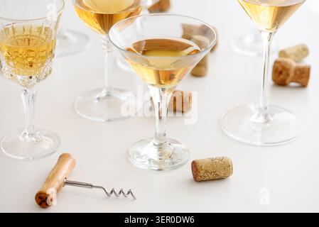 Glasses of white wine standing on a white table, surrounded by wine corks and a corkscrew, representing entertaining, celebration, and elegant tasting Stock Photo