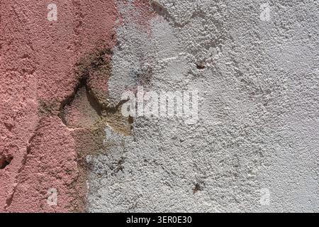 Aged plaster wall shows peeling surfaces, exposed layers, and rough texture in pink and white tones. Stock Photo