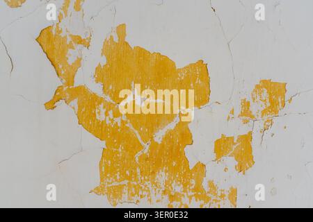 Cracked white paint flakes away to reveal a vibrant yellow layer on a weathered wall surface. Stock Photo