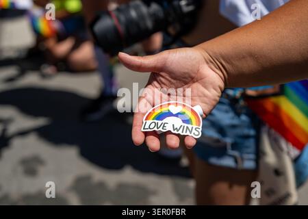 Close up view of a person holding out a rainbow sticker reading Love Wins in their hand during an outdoor Gay Pride March celebration. Stock Photo