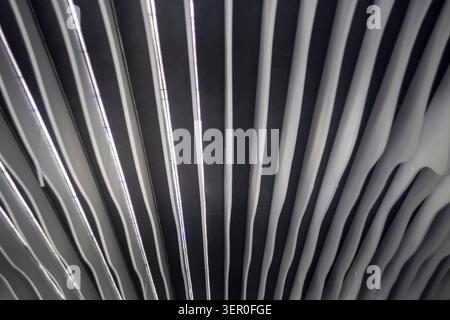 An abstract full frame background of a contemporary interior ceiling featuring dynamic white wavy panels arranged in parallel lines with built in line Stock Photo