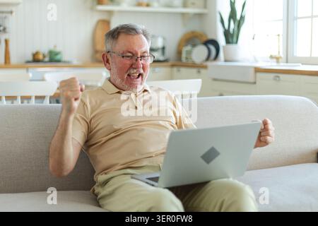 Excited middle aged senior man euphoric winner. Older mature grandfather looking at laptop reading great news getting good result winning online bid feeling amazed. Winning gesture Stock Photo