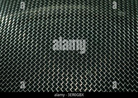 Close macro photograph of a shiny woven metal mesh or kitchen strainer, with diagonal lines, reflections and a clean abstract pattern. Stock Photo