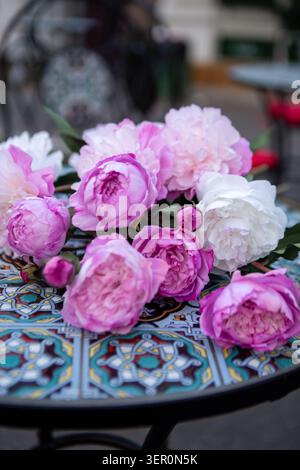 A group of faux peonies with pink and white blooms sits on a colorful table with intricate designs. The scene shows an inviting atmosphere with nearby Stock Photo