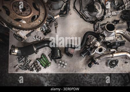 A collection of disassembled car engine parts, including a flywheel, turbocharger components, hoses, and various bolts, are neatly arranged on a textu Stock Photo