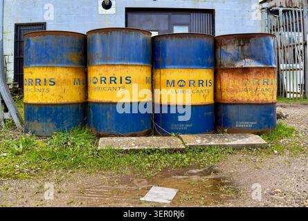 Four rusty Morris Lubricants blue & yellow oil drums standing outside an industrial building Stock Photo