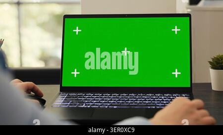 Female manager works on laptop running isolated green screen template, checking pc with blank mockup display Stock Photo