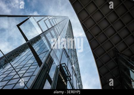 Construction workers and engineers are working on a tall glass building in the city. The sky is cloudy and the building reflects the surrounding area. Stock Photo
