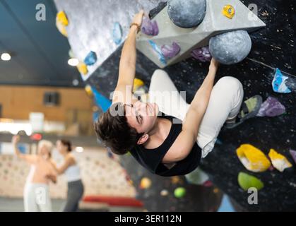 Determined young man doing his best at climbing artificial wall Stock Photo