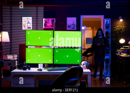 Hacker entering RGB lit apartment with mockup multi monitor setup, working on building stealth malware. Stock Photo