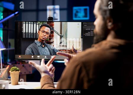 IT admin working from home in videocall with african american coworker, testing programs and systems. Programmer checking code with colleague in online teleconference, sitting at desk in apartment. Stock Photo