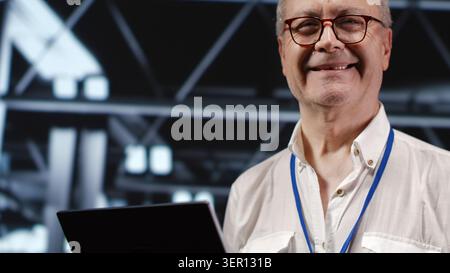 Adept IT professional navigating network of servers in industrial workspace, engineer with laptop in hand ensuring seamless operations, doing optimizations and maintenance in data center Stock Photo