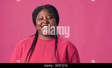 Video showcasing stylish African American woman with penchant for pink sweater fashion confidently striking poses, genuine laughter of young lady infuses authentic charm to the close-up shot. Stock Photo