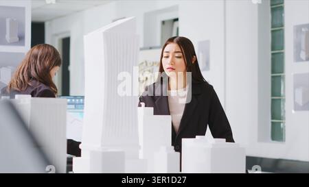 Architect analyzing blueprints and 3d building models at design table, trying to develop new industrial plan for residential area project. Stock Photo