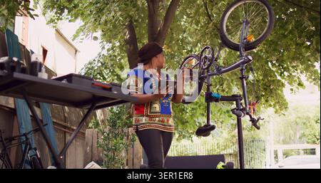 Dedicated African American lady using phone tablet to research for solutions of damaged bike tire in yard. Stock Photo