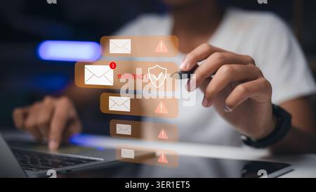 person holding stylus pen near virtual email notifications with warning sign and shield icon. Concept of cyber security, phishing awareness, spam aler Stock Photo