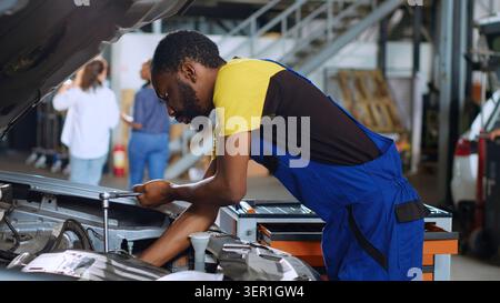 Trained engineer in car service uses torque wrench to tighten bolts inside vehicle after fixing components inside, African American repair shop expert utilizes professional tools to mend automobile. Stock Photo