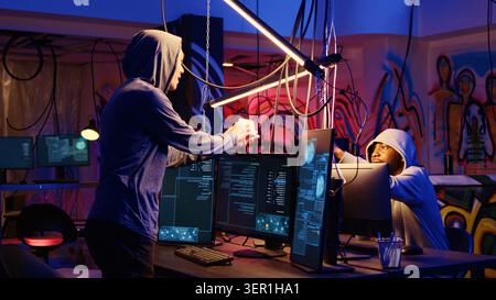 Hacker in hidden bunker uploading script on SSD that can launch DDoS attacks on any website, excited to show it to colleague. Stock Photo