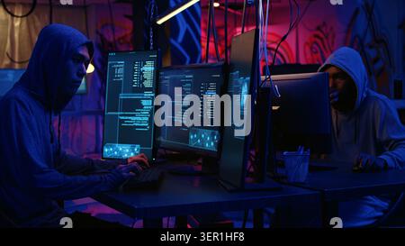 Hackers in dark abandoned warehouse using phishing technique that tricks users into revealing sensitive information, rogue developers stealing passwords from low security systems, dolly in shot. Stock Photo