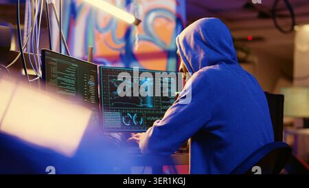 African American hooded hacker hiding in underground base, anxiously looking around for threats, feeling nervous after stealing data from victims using virus, trying hard to evade law enforcement. Stock Photo