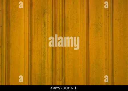 A close-up full-frame background shot of a weathered yellow corrugated zinc or steel sheet fence, showing vertical ridges, and dirt stains. Stock Photo