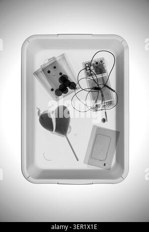 X-ray of items on an airport scanner tray including a wallet with coins, a passport, a heart-shape lolly and a mobile phone with earphones. Stock Photo
