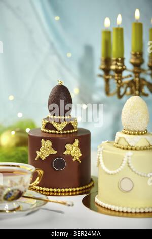 Two beautifully decorated easter cakes topped with chocolate eggs, golden angels, and beads, creating a luxurious and elegant festive scene Stock Photo