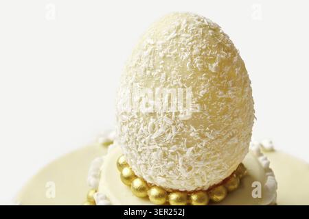 Close-up of a white chocolate easter egg covered in shredded coconut, sitting on a beautifully decorated cake Stock Photo