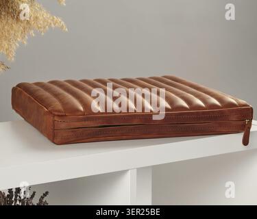 Closed brown leather laptop sleeve with zipper closure resting on a white shelf, showcasing its sleek and protective design Stock Photo