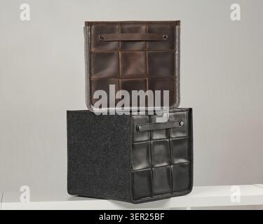 Two elegant storage boxes made of leather and felt, placed on a white shelf, offer a modern and organized storage solution Stock Photo