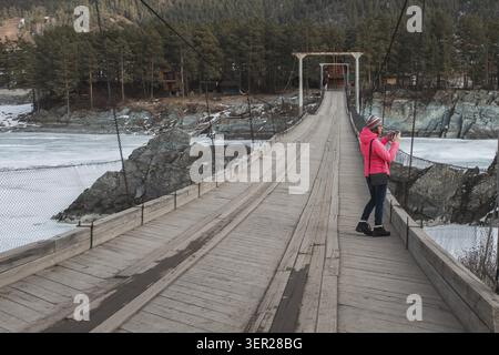 Happy woman taking photos on the bridge from river at beauty sunny spring day, in Altai mountains. Travel vacation concept Stock Photo