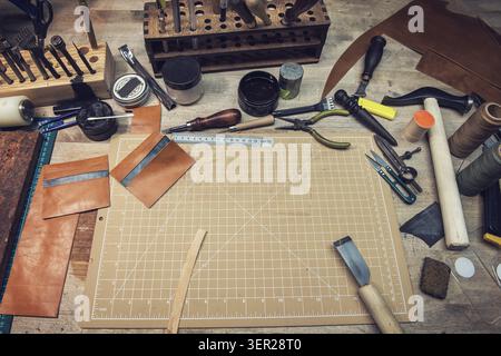 Leathermaker's work desk. Tools and leather at cobbler workplace. Tools for craft production of leather goods on wooden table Stock Photo