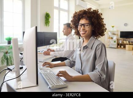 Smiling female software developer coding at desktop in bright modern office Stock Photo
