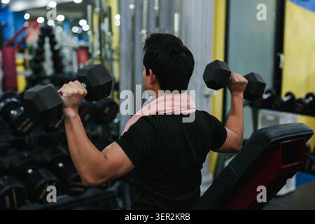 Asian man doing dumbbell shoulder press in gym for strength training workout fitness Stock Photo