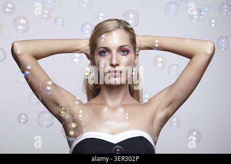 Beautiful young blonde woman with soap bubbles. Female on grey background with hands up Stock Photo