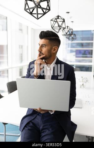 Thoughtful Indian businessman working on laptop in office Stock Photo