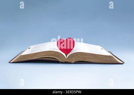 Open bible with a red heart at the center of the pages. Isolated on light blue background. Stock Photo