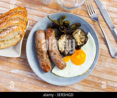 Tasty grilled sausages served with fried eggs, pepper and eggplant Stock Photo