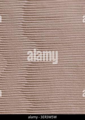 Close-up of a beige ribbed knit fabric showing horizontal ribs, fine yarn texture, and a gentle vertical fold. Soft matte surface with even studio lig Stock Photo