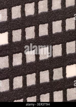 Macro view of a patterned surface showing a black felt-like grid with regularly spaced white granular square inserts. Soft diffuse lighting highlights Stock Photo