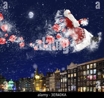 Santa claus is flying with snow and gift boxes on deep red background Stock Photo