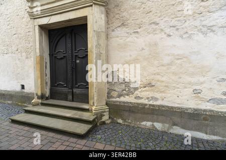 An old historic building has a dark wooden door with steps leading up to it. The wall beside the entrance shows signs of age and wear. The ground is m Stock Photo