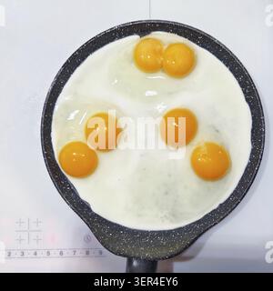 Delicious double-yolk eggs being fried in a non-stick pan, viewed from above, on a stovetop on induction cooker stove Stock Photo