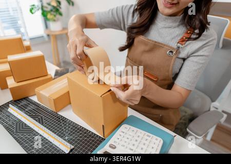 Small business owner preparing customer orders by packing boxes, checking products, recording shipment details and managing online sales in a home off Stock Photo