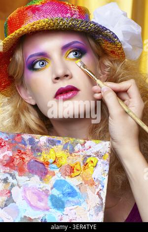 Artist's hand with paintbrush painting beautiful girl's colorful eye shadow make up using palette Stock Photo