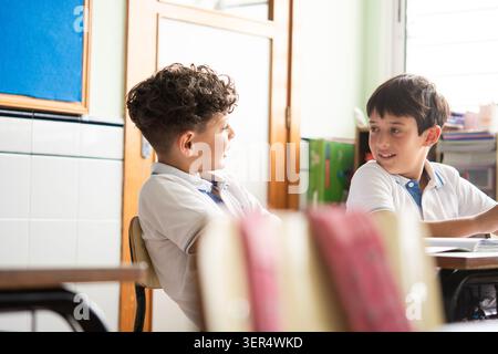 Two primary school students sitting at their desks and interacting during class time. Stock Photo