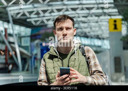 Young male traveler using smartphone inside modern airport terminal before flight departure Stock Photo