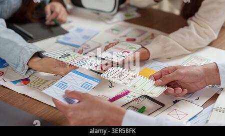 Cropped hands of designers comparing mobile app paper wireframes for UX UI prototyping Stock Photo