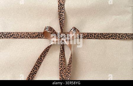 Brown gift box wrapped in kraft paper with a leopard print ribbon bow, showcasing a stylish and elegant presentation  Stock Photo