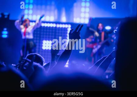 Enthusiastic concertgoers with hands in the air, cheering on musicians performing live on stage under vibrant blue lighting Stock Photo